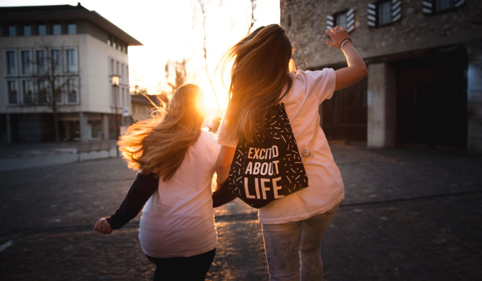 Two young women linking arms skipping into the sunset