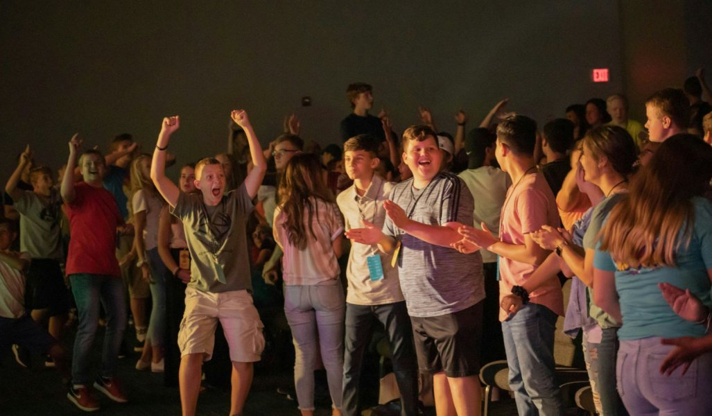 Middle Schoolers in auditorium audience laughing, jumping, clapping hands and cheering