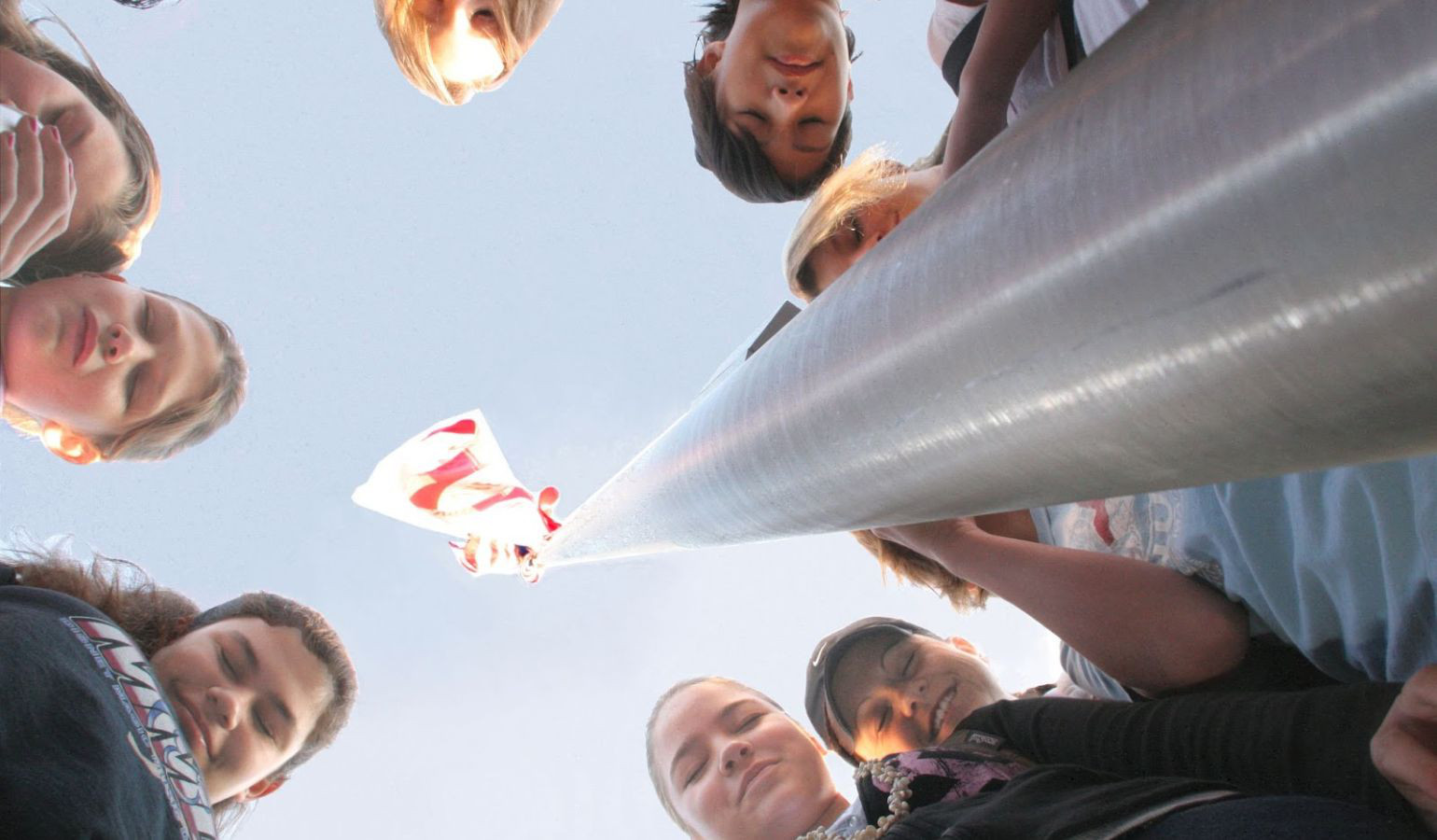 Picture taken from the ground looking up to students praying around a flag ple