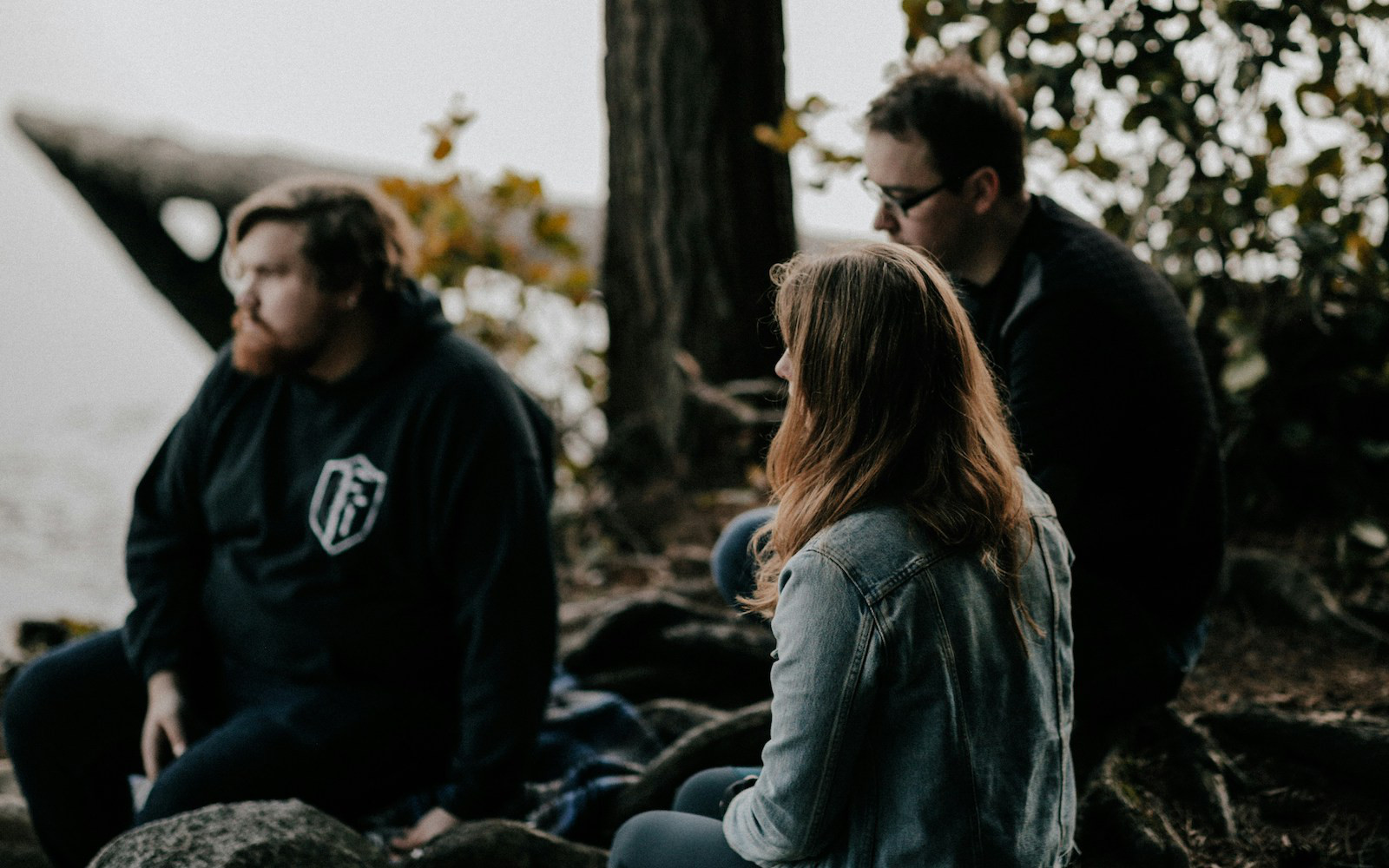 Three white young adults gathered sitting in nature