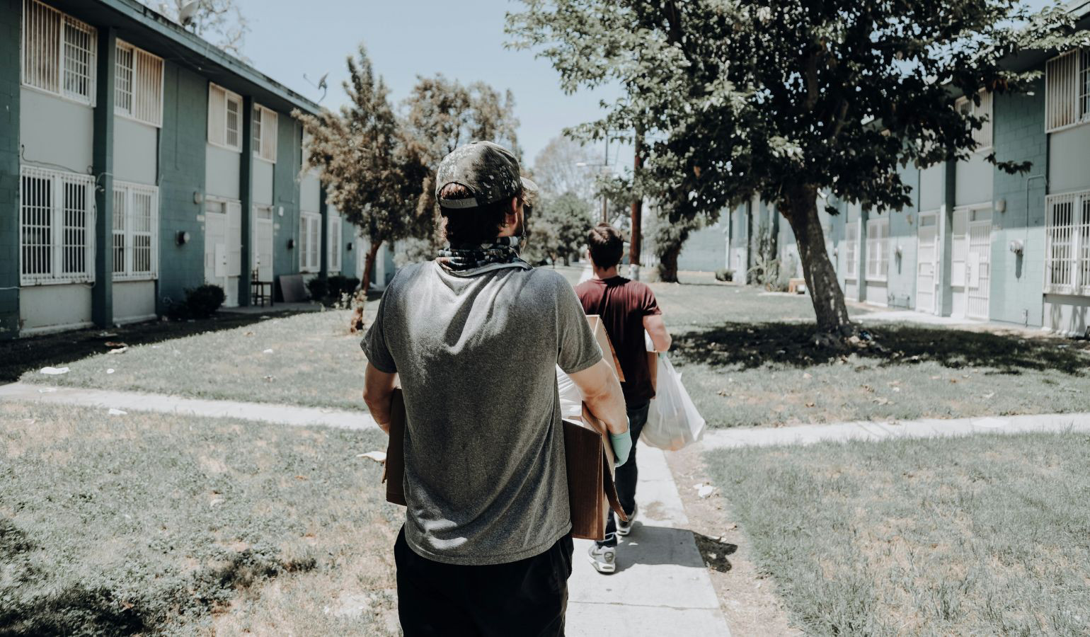 Two young men carrying boxes down an apartment complex pathway