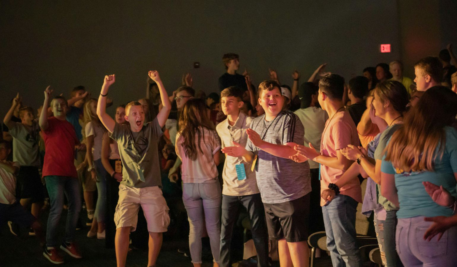 Middle Schoolers in auditorium audience laughing, jumping, clapping hands and cheering