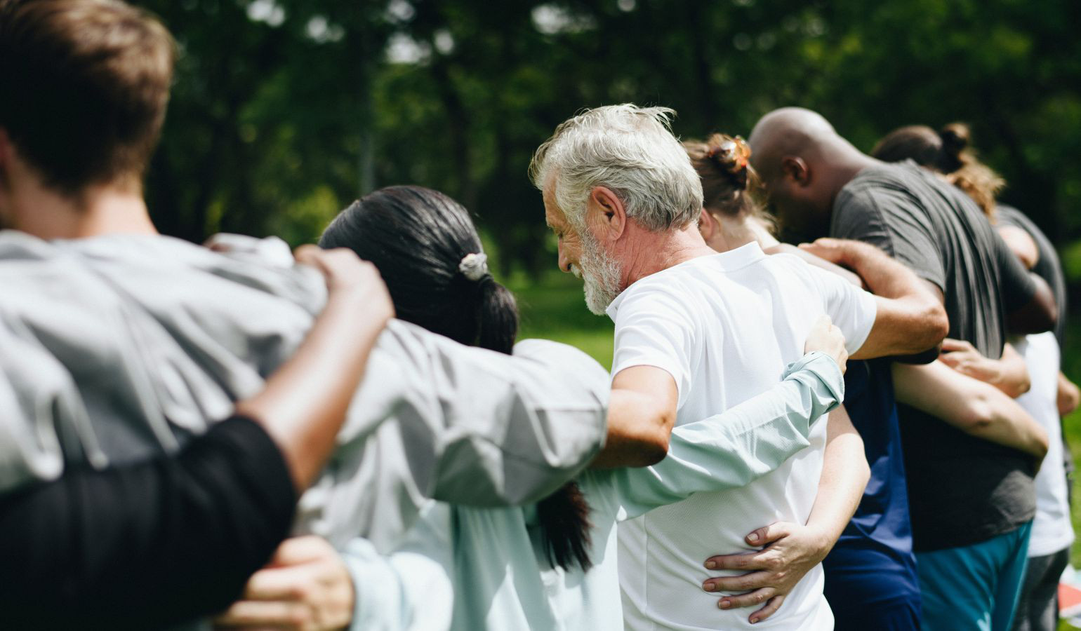 Youth and youth leaders linking arms and praying. Point of view, watching from behind.