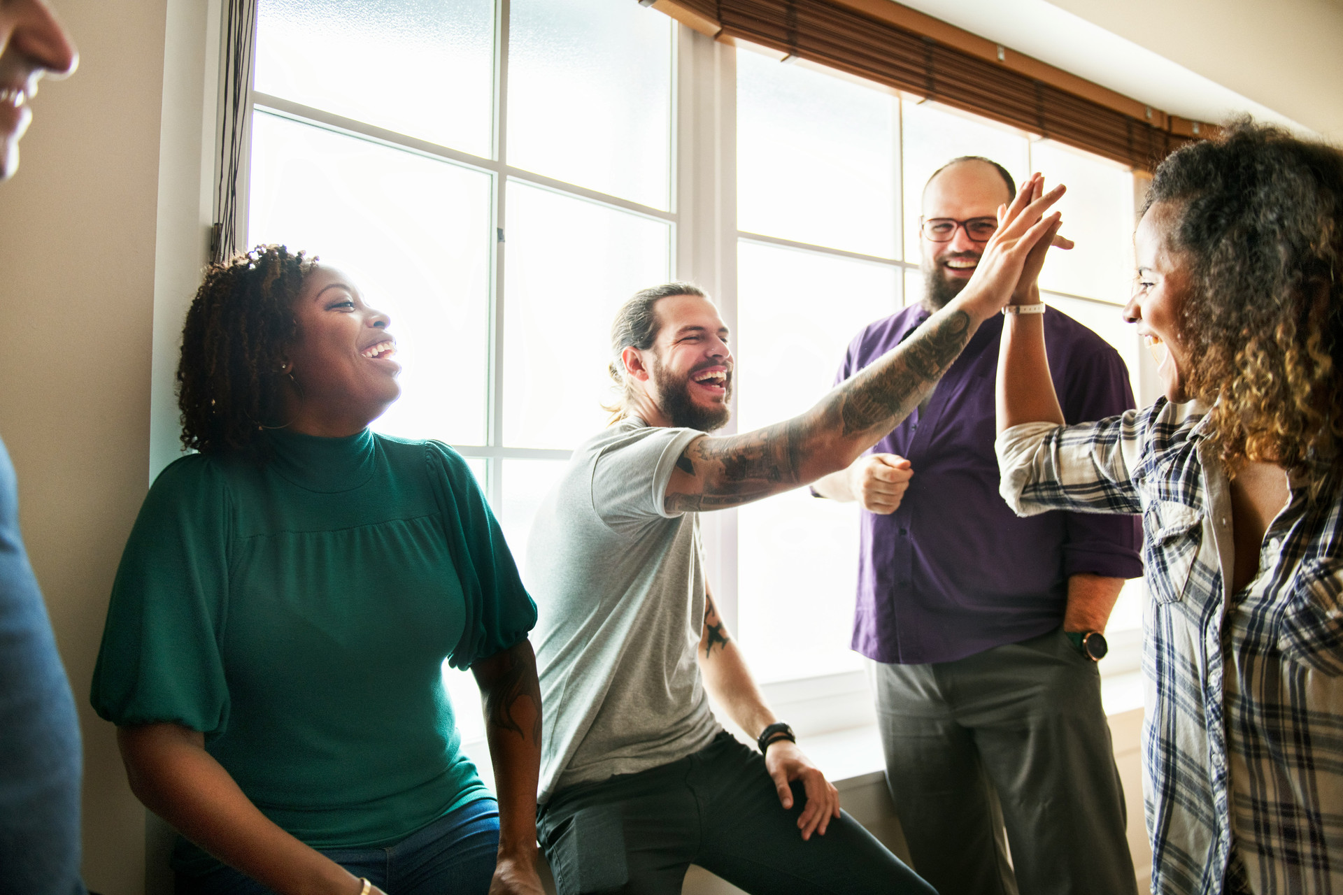 Multiracial young adults laughing and high fiving by a window