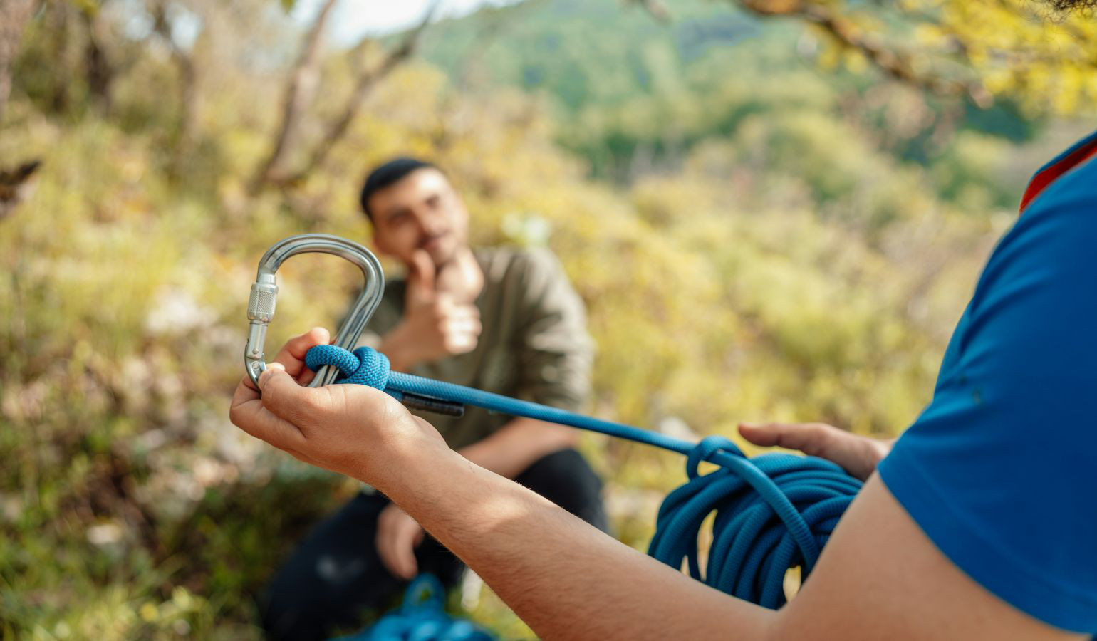 Young man preparing a rope and carabiner clip on a mountain.