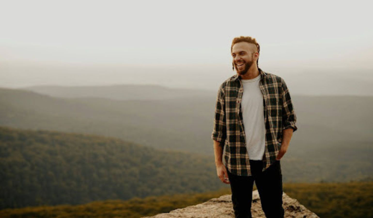 Young man standing on a rock with a foggy view smiling