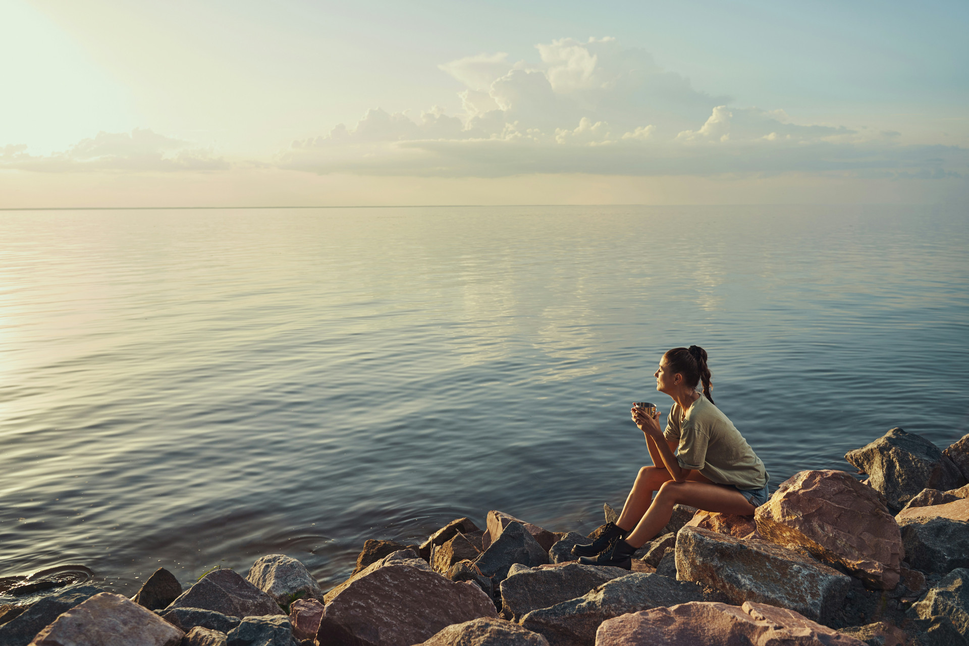 Young woman sitting next to calm, stil lake in the early morning light