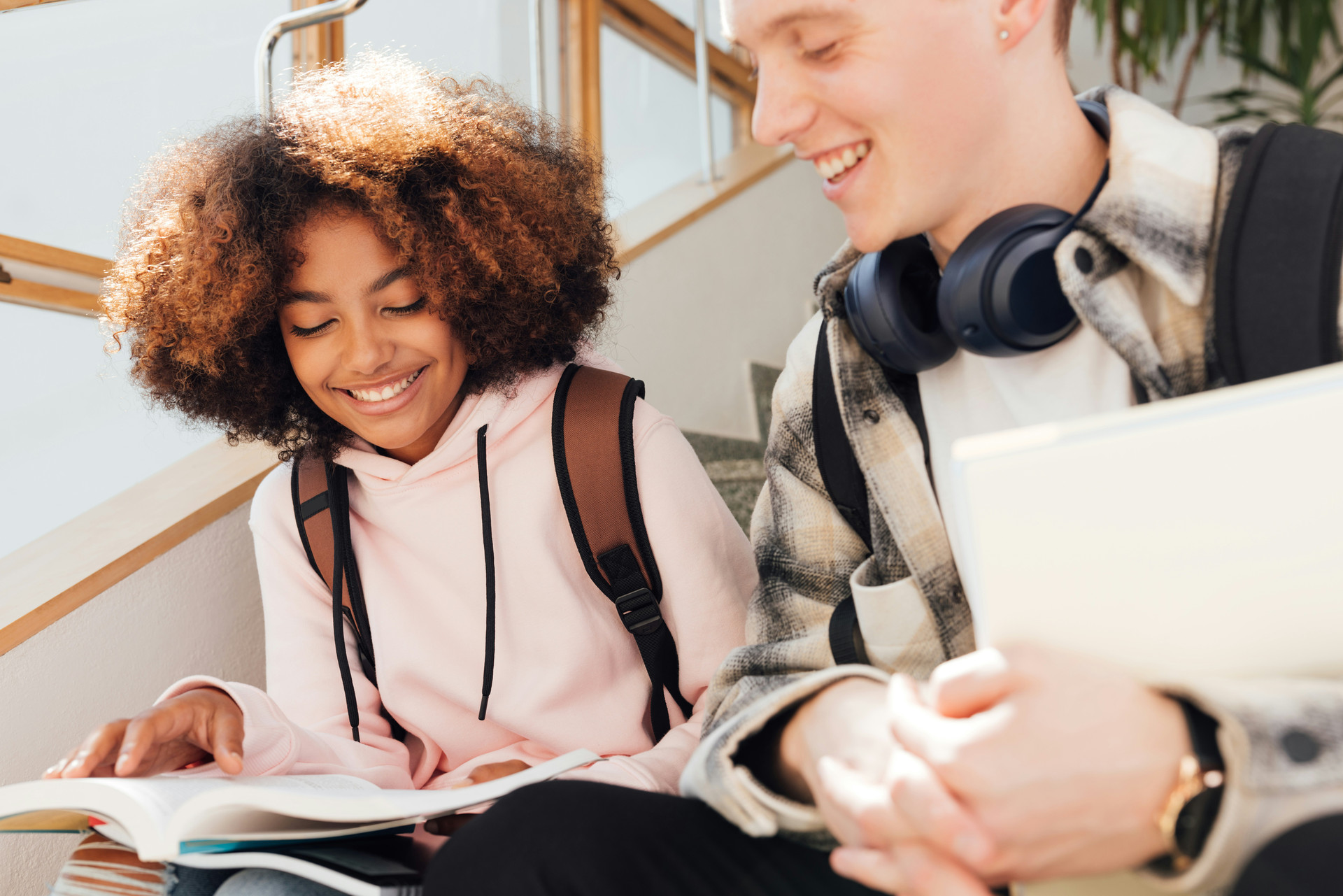Young black female and white male students on stairs showing each other schoolwork