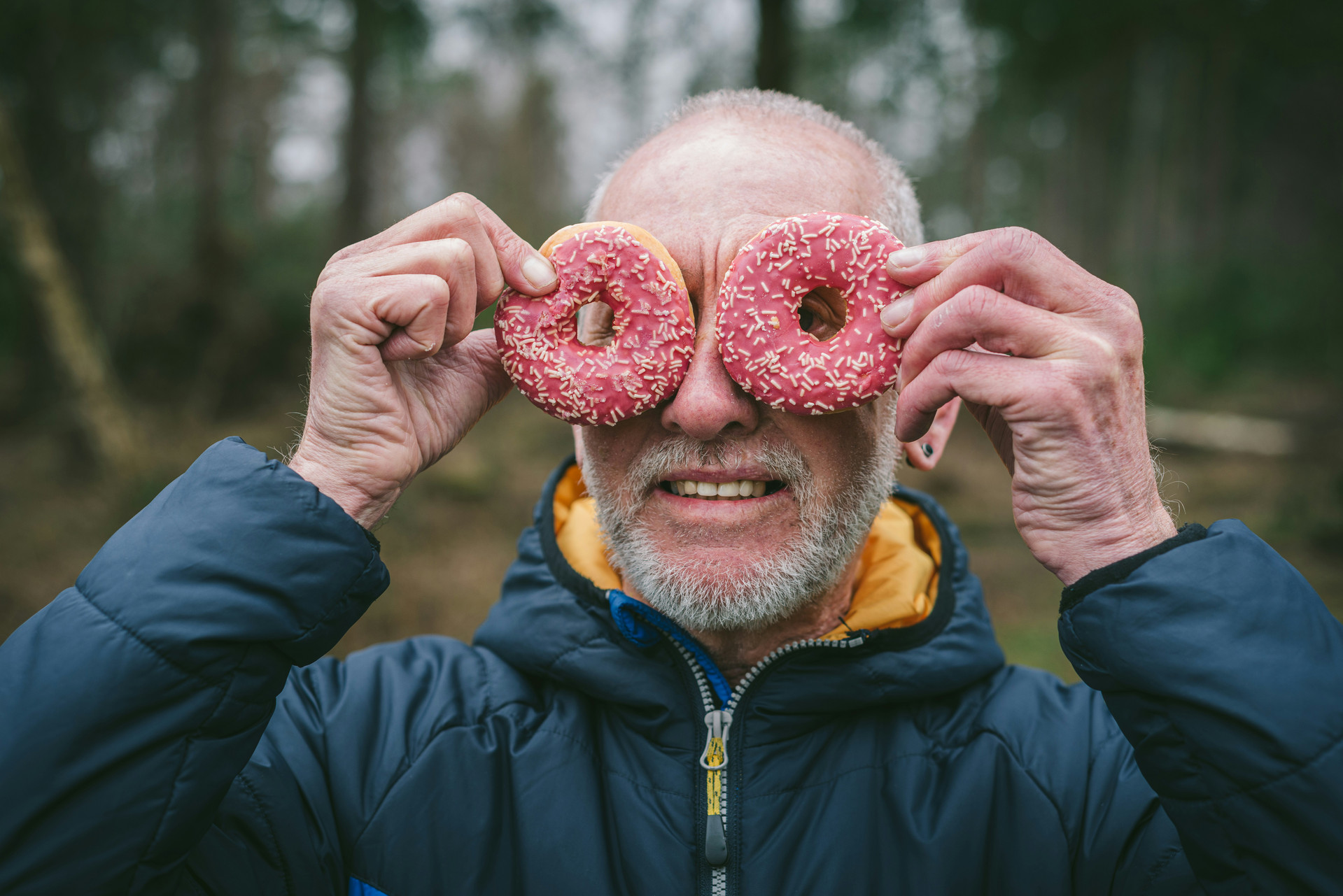 Older gentleman holding up pink sprinkle donuts to his eyes