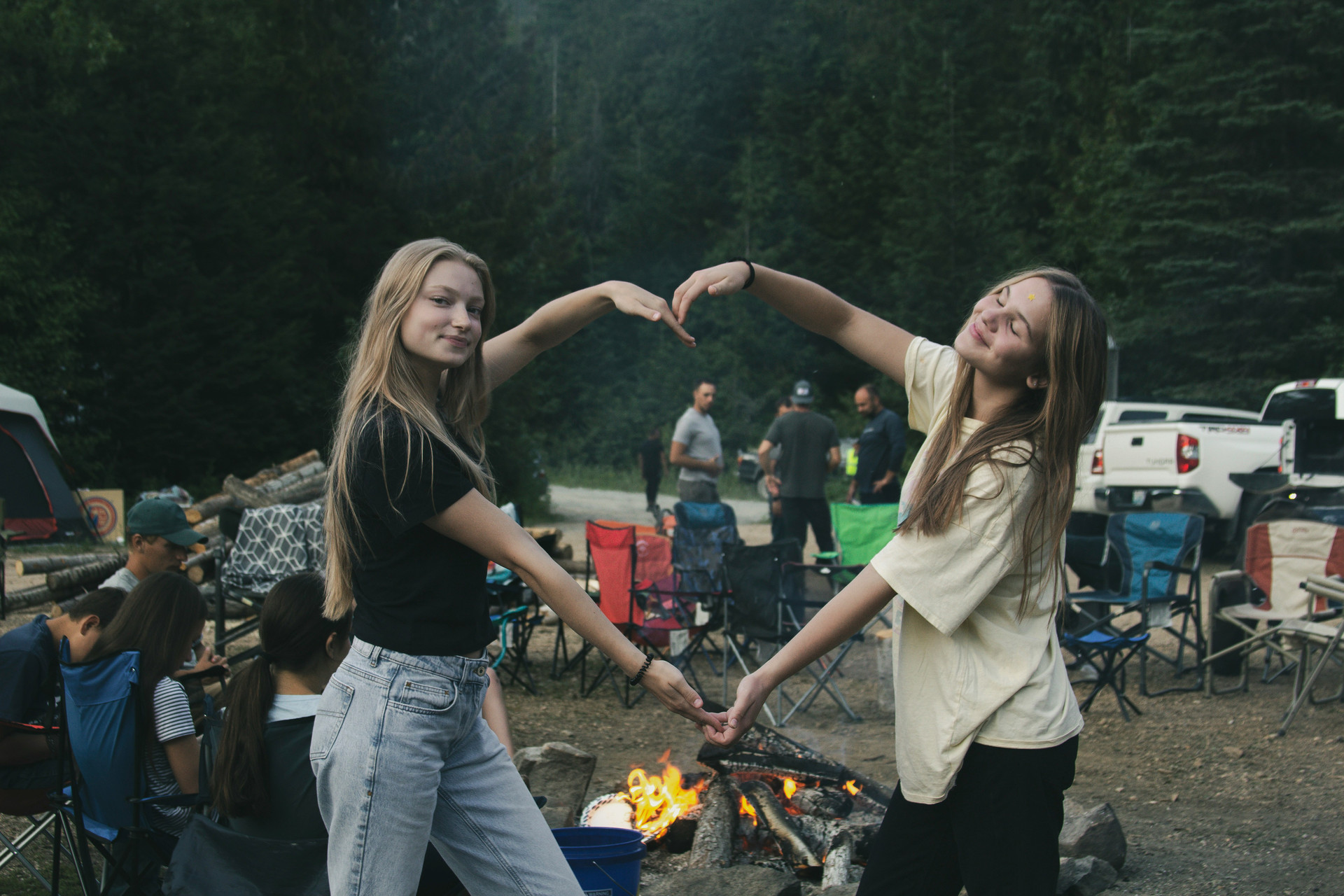 Female students making a heart with their arms in front of a campfire.