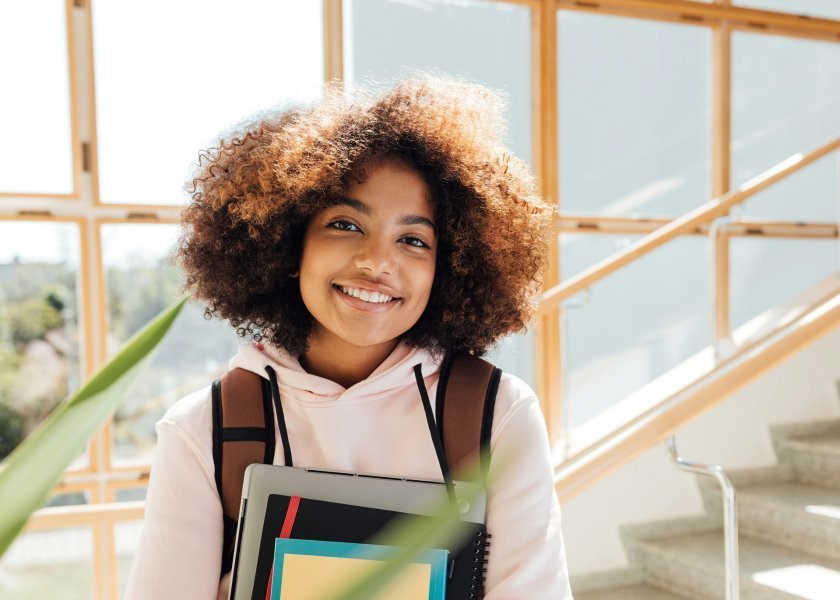 Student at school stairs holding her books and smiling