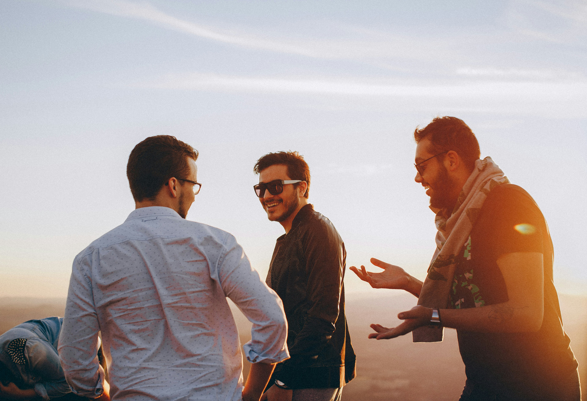 Three male friends laughing at sunset