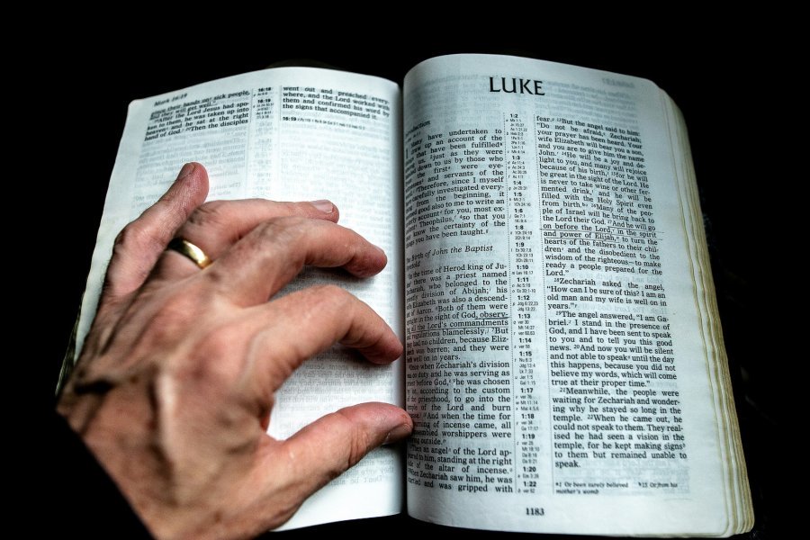 Bible open to Luke, with hand over it