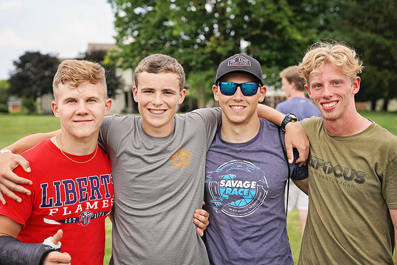 Four teenage boys with their arms around each other smiling